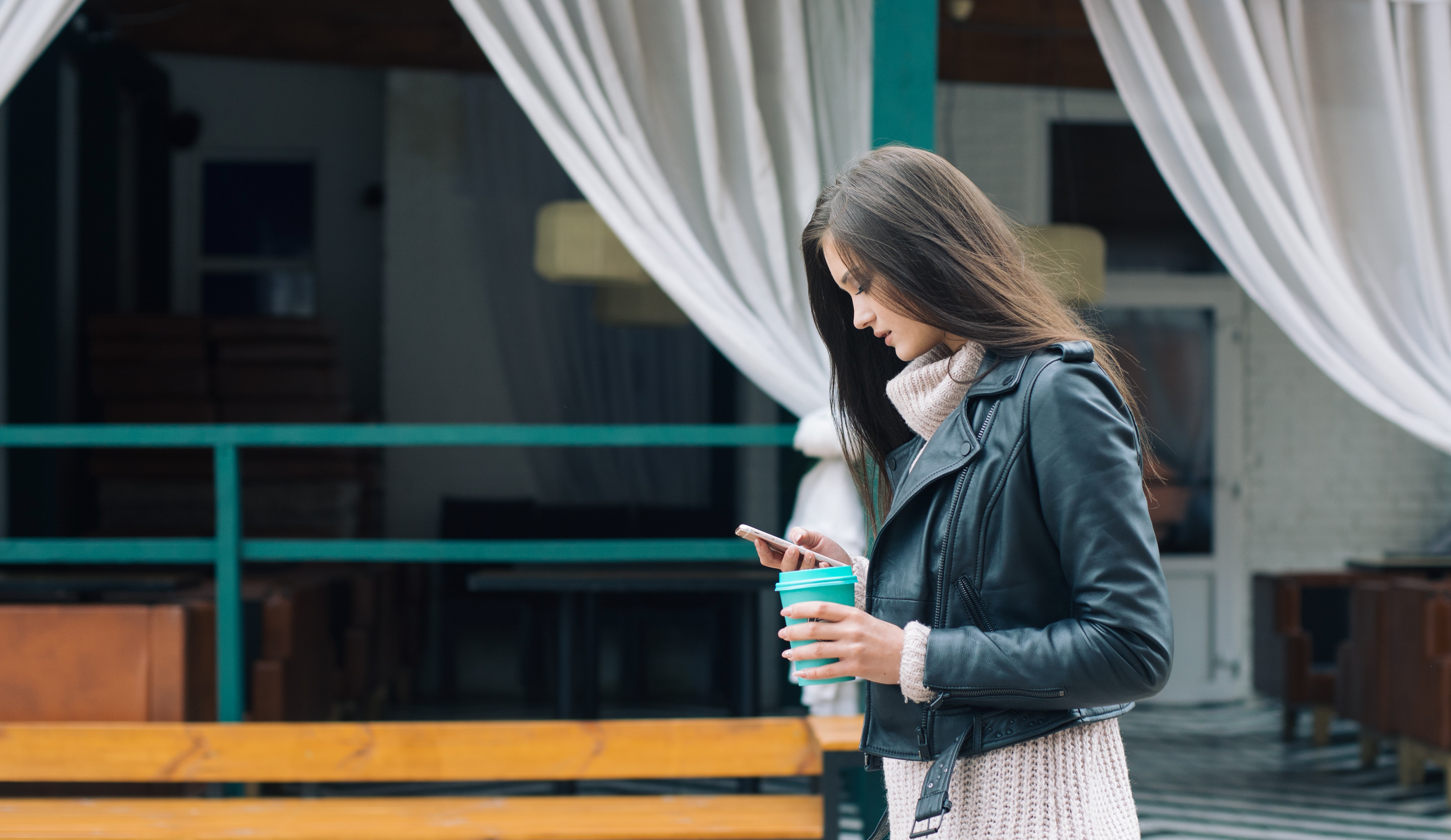 Woman holding coffee in her left hand looking at her phone in her right hand