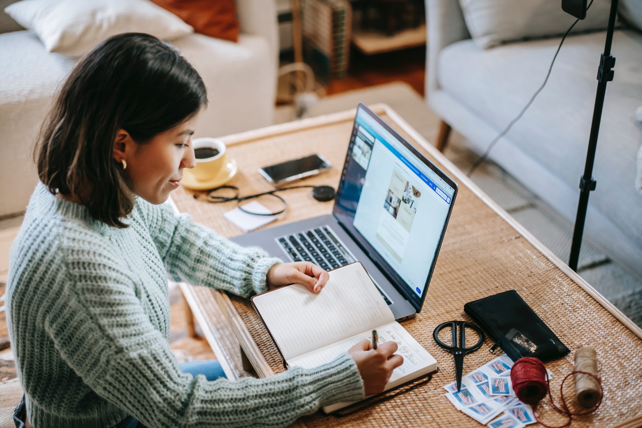 Woman with laptop in front of her taking notes in a notebook