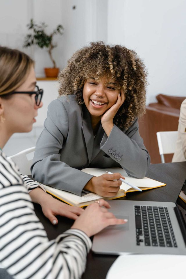 woman smiling and looking at her collegue explain somthing of the laptop