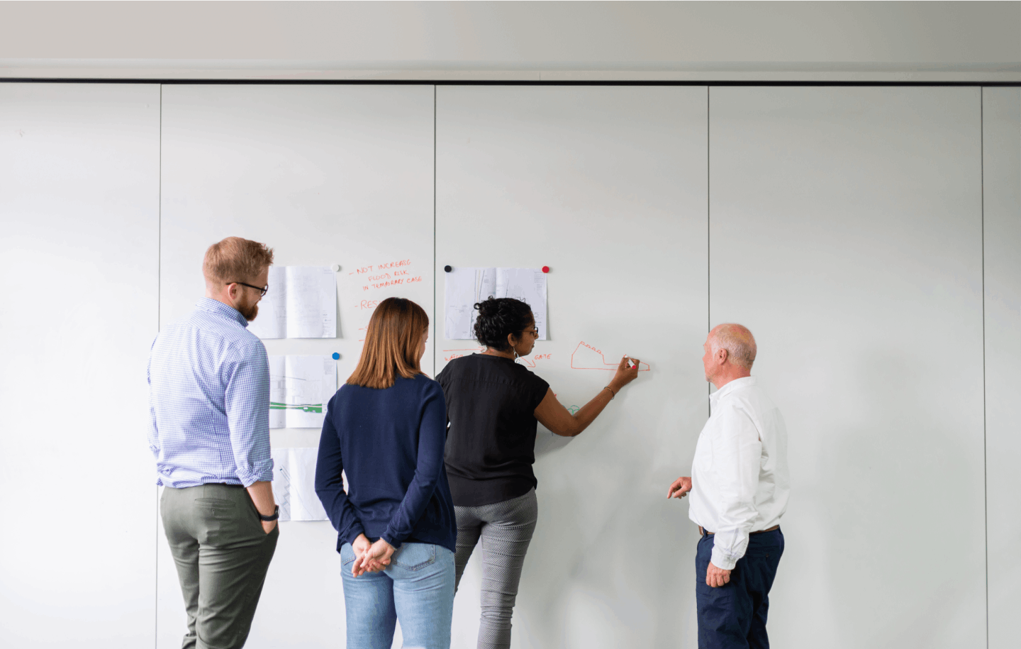 One person showing a graph on a white board to three people who are standing around them