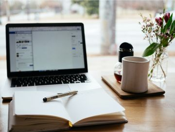 A desk with a notebook open in front of a laptop