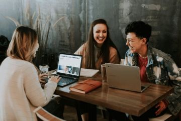 Three people around a table looking at laptops and talking