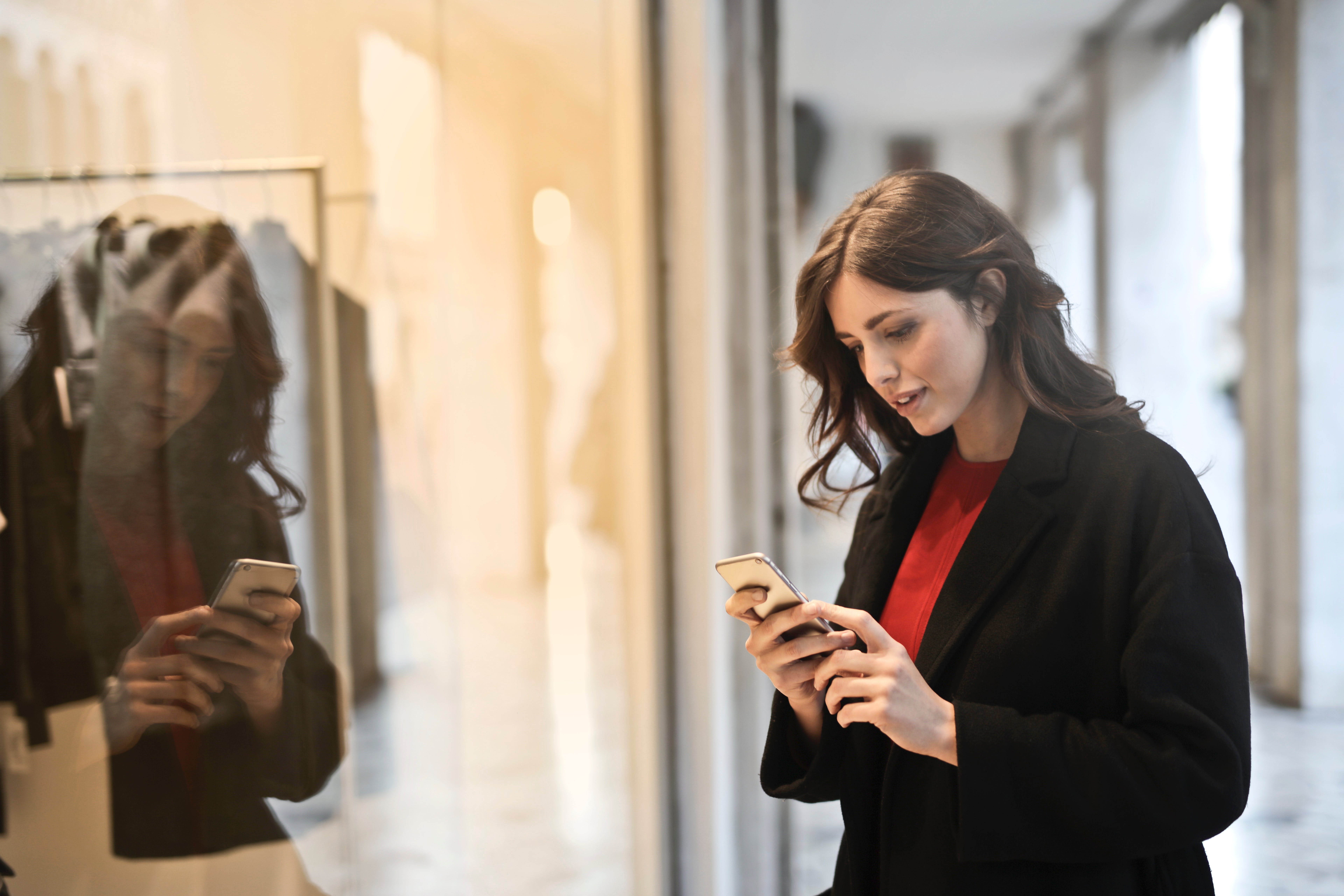 Woman holding a phone in her hand standing in front of a store window