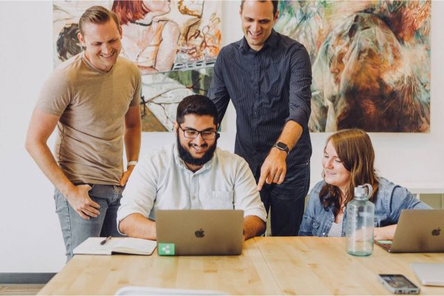 Four people sitting at a table looking at a laptop